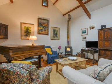 A living room with a piano armchairs a wood stove and a coffee table at Townend Barn in Lydford