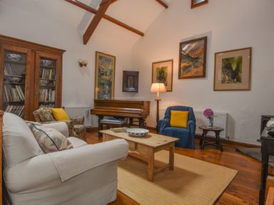 A living room with a piano a wooden coffee table and armchairs at Townend Barn in Lydford