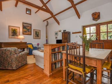 A living room with wooden beams wooden dining table flowers on table and bookshelf at Townend Barn in Lydford
