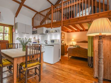A small kitchen and dining area with a wooden table and chairs next to a bedroom with a bed and bedside lamps at Townend Barn in Lydford
