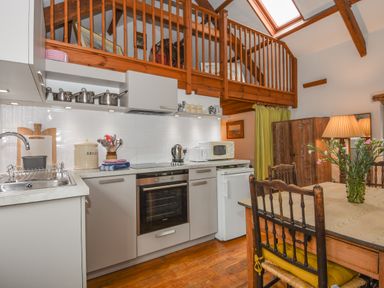 A kitchen with white cabinets a dining table with chairs and flowers in a vase at Townend Barn in Lydford