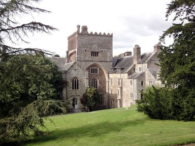 A historic stone building with large windows and a tower surrounded by trees and grass at Burham Barn in Dousland near Yelverton