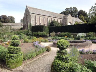 A formal garden with trimmed bushes and flower beds in front of a large stone building at Burham Barn in Dousland near Yelverton