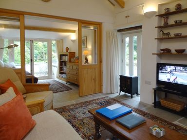 A living room with sofa chairs coffee table television and shelves at Burham Barn in Dousland near Yelverton