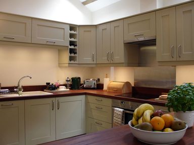 A kitchen with beige cabinets wooden countertops a bowl of fruit and a potted plant at Burham Barn in Dousland near Yelverton