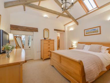 A bedroom with a wooden bed chest of drawers a dressing table and a TV at Burham Barn Dousland near Yelverton