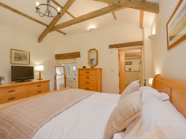A bedroom with a wooden bed beside a dresser with a television and a mirror at Burham Barn in Dousland near Yelverton