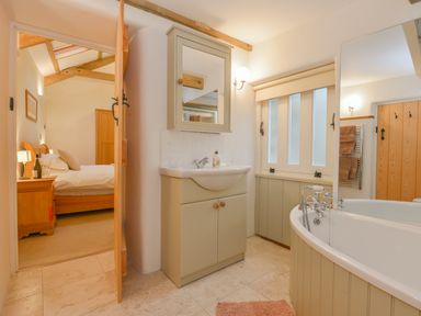 A bathroom with a sink cabinet and a bathtub next to a window and an open door leading to a bedroom at Burham Barn in Dousland near Yelverton