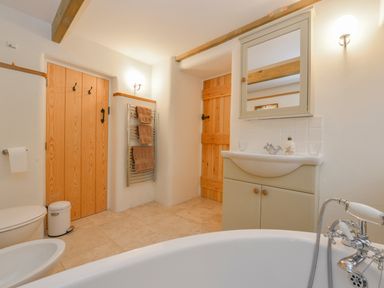 A bathroom with a bathtub in the foreground a sink cabinet with mirror wooden doors towel rack and toilet at Burham Barn in Dousland near Yelverton