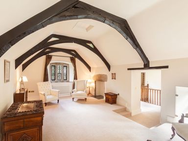 An attic room with exposed dark wooden beams two armchairs and a small fireplace at Great Bidlake Manor in Bridestowe near Lydford