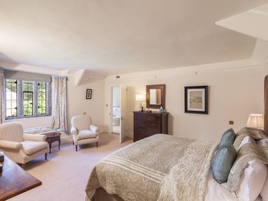 A bedroom with a bed two armchairs a wooden dresser and a window at Great Bidlake Manor in Bridestowe near Lydford