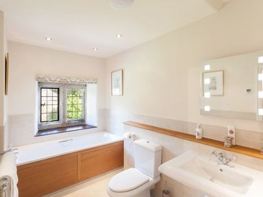A bathroom with a bathtub under a window a toilet and a sink with a mirror above at Great Bidlake Manor in Bridestowe near Lydford