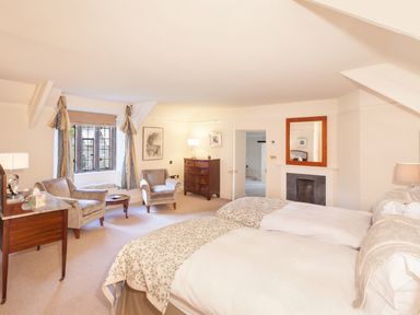 A bedroom with two beds a wooden dresser two upholstered chairs a window with curtains and a fireplace at Great Bidlake Manor in Bridestowe near Lydford