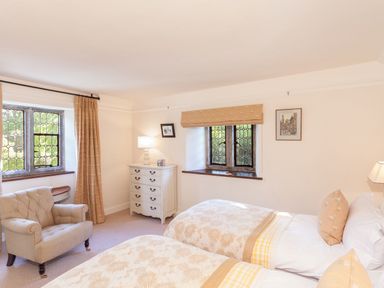 A bedroom with two single beds a beige armchair a white chest of drawers and two leaded glass windows at Great Bidlake Manor in Bridestowe near Lydford