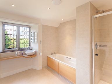 A bathroom with a bathtub wooden panel shower enclosed with glass and sink under window at Great Bidlake Manor in Bridestowe near Lydford