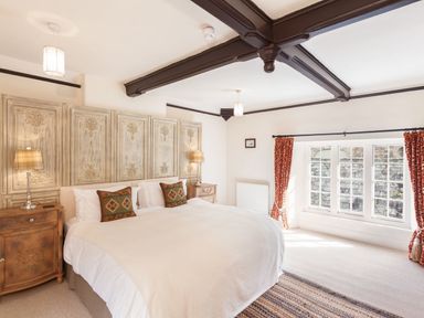 A bedroom with a large bed two nightstands with lamps exposed ceiling beams and large windows with red curtains at Great Bidlake Manor in Bridestowe near Lydford