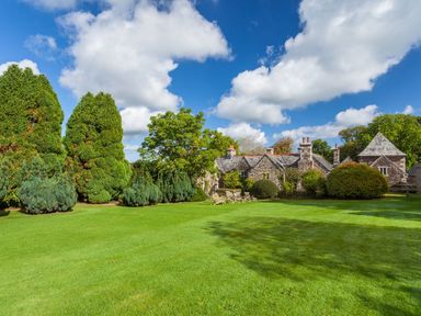 A large lawn with trees and a stone house in the background at Great Bidlake Manor in Bridestowe near Lydford
