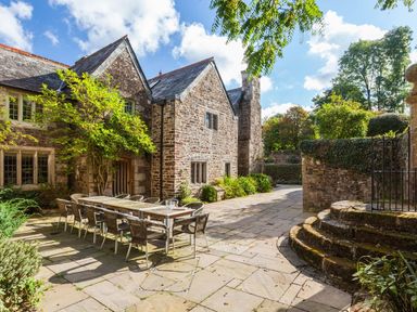 An outdoor patio area with a long dining table and chairs next to a stone building at Great Bidlake Manor Bridestowe near Lydford