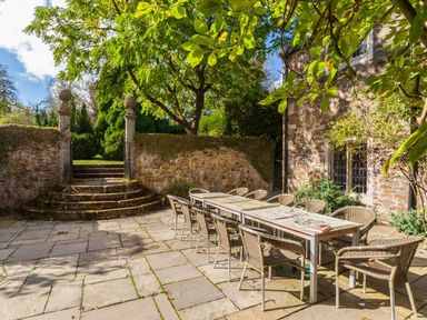 An outdoor stone patio with a long table and chairs near a stone building at Great Bidlake Manor Bridestowe near Lydford