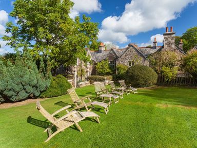 A lawn with wooden lounge chairs and trees in front of a stone house at Great Bidlake Manor Bridestowe near Lydford