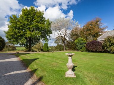 A garden with a sundial on a lawn and various trees near a gravel path at Great Bidlake Manor Bridestowe near Lydford