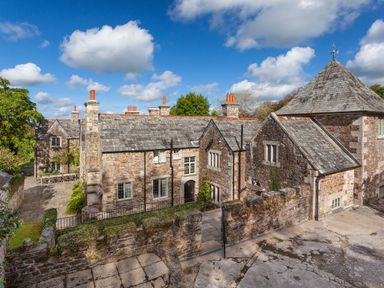 A stone manor house with multiple chimneys and a slate roof under a blue sky at Great Bidlake Manor Bridestowe near Lydford