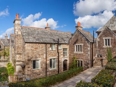 An exterior view of a stone building with multiple chimneys and windows surrounded by greenery at Great Bidlake Manor in Bridestowe near Lydford