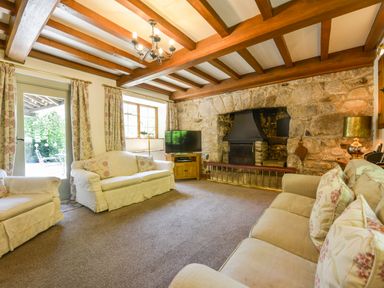 A living room with sofas a stone fireplace wooden beams and a television at Bagtor Mill in Ilsington near Haytor Vale