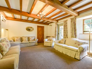 A living room with three sofas with floral cushions wooden beams on ceiling and a wooden door at Bagtor Mill in Ilsington near Haytor Vale