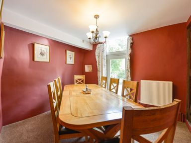 A dining room with wooden table and chairs red walls and floral curtains at Bagtor Mill Ilsington near Haytor Vale