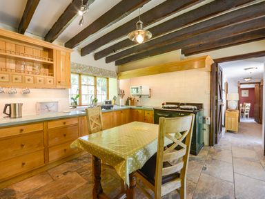 A kitchen with wooden cabinets a table with chairs and visible beams on the ceiling at Bagtor Mill Ilsington near Haytor Vale