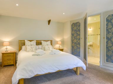 A bedroom with a wooden bed with white bedding and patterned pillows two bedside tables with lamps and an open door leading to a bathroom at Bagtor Mill in Ilsington near Haytor Vale