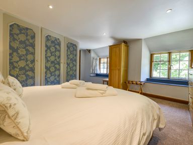 A bedroom with a bed towels wardrobe and windows at Bagtor Mill in Ilsington near Haytor Vale
