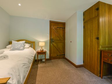 A bedroom with a single bed, bedside table with lamp, wooden door, built-in wooden wardrobe and carpet flooring at Bagtor Mill in Ilsington near Haytor Vale