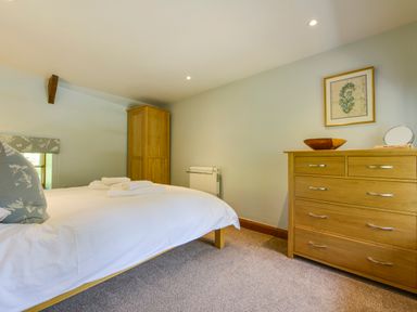 A bedroom with a bed towels wooden wardrobe and dresser with framed picture at Bagtor Mill in Ilsington near Haytor Vale
