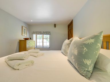 A bedroom with a bed with folded towels pillows a window and a wooden chest of drawers at Bagtor Mill in Ilsington near Haytor Vale