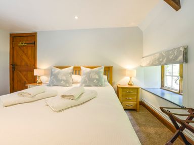 A bedroom with a bed towels bedside tables lamps window and wooden door at Bagtor Mill in Ilsington near Haytor Vale