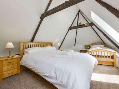 A bedroom with two wooden beds bedside tables and lamps under a pitched ceiling with exposed beams at Bagtor Mill in Ilsington near Haytor Vale