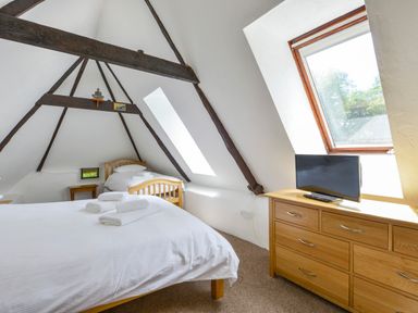 A bedroom with a large bed and a single bed under a pitched roof with wooden beams and a window at Bagtor Mill in Ilsington near Haytor Vale