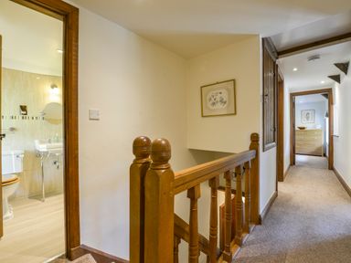 A hallway with carpeted floor wooden railing and doorway to a bathroom with toilet and sink at Bagtor Mill in Ilsington near Haytor Vale