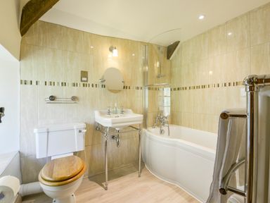 A bathroom with a toilet with wooden seat a sink a bathtub with shower and a towel rack at Bagtor Mill in Ilsington near Haytor Vale