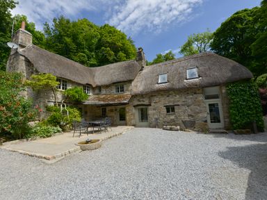 An exterior view of a stone thatched roof cottage with patio furniture and plants at Bagtor Mill in Ilsington near Haytor Vale