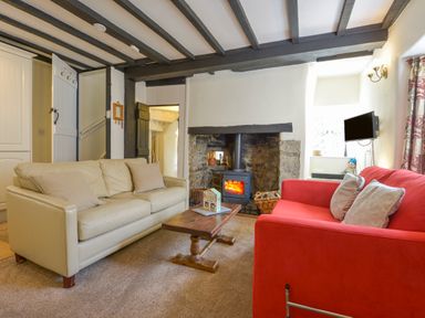 A living room with a beige sofa a red sofa a wood burning stove and a wooden coffee table at Little Gate Cottage in North Bovey