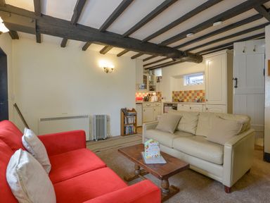 A living room with red and beige sofas and a wooden coffee table near a kitchen with white cabinets at Little Gate Cottage in North Bovey