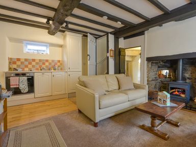 A living room with a cream sofa wooden coffee table and fireplace with a stove at Little Gate Cottage in North Bovey