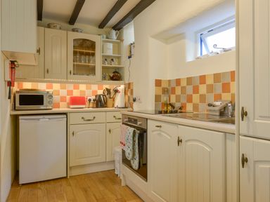 A kitchen with cream cabinets a microwave oven stove and tiled backsplash at Little Gate Cottage in North Bovey