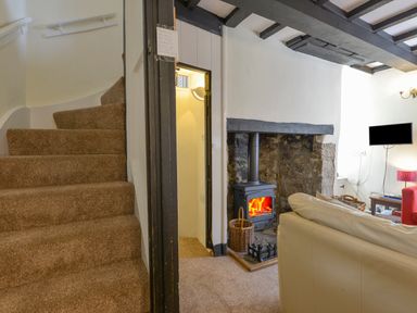 A living room with a carpeted staircase a wood burning stove in a stone fireplace a white sofa and a wall mounted tv at Little Gate Cottage in North Bovey