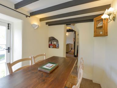 A dining area with a wooden table and chairs under exposed ceiling beams at Little Gate Cottage North Bovey