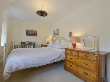 A bedroom with a bed table lamps a wooden dresser and a bookshelf at Little Gate Cottage in North Bovey