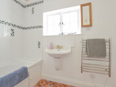 A bathroom with a bathtub, a sink, a towel rail with a grey towel, and a window above the sink at Little Gate Cottage in North Bovey